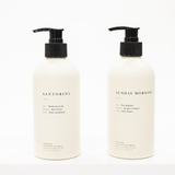 Two white bottles with black pump caps labeled 'Santorini' and 'Sunday Morning' on a white background.