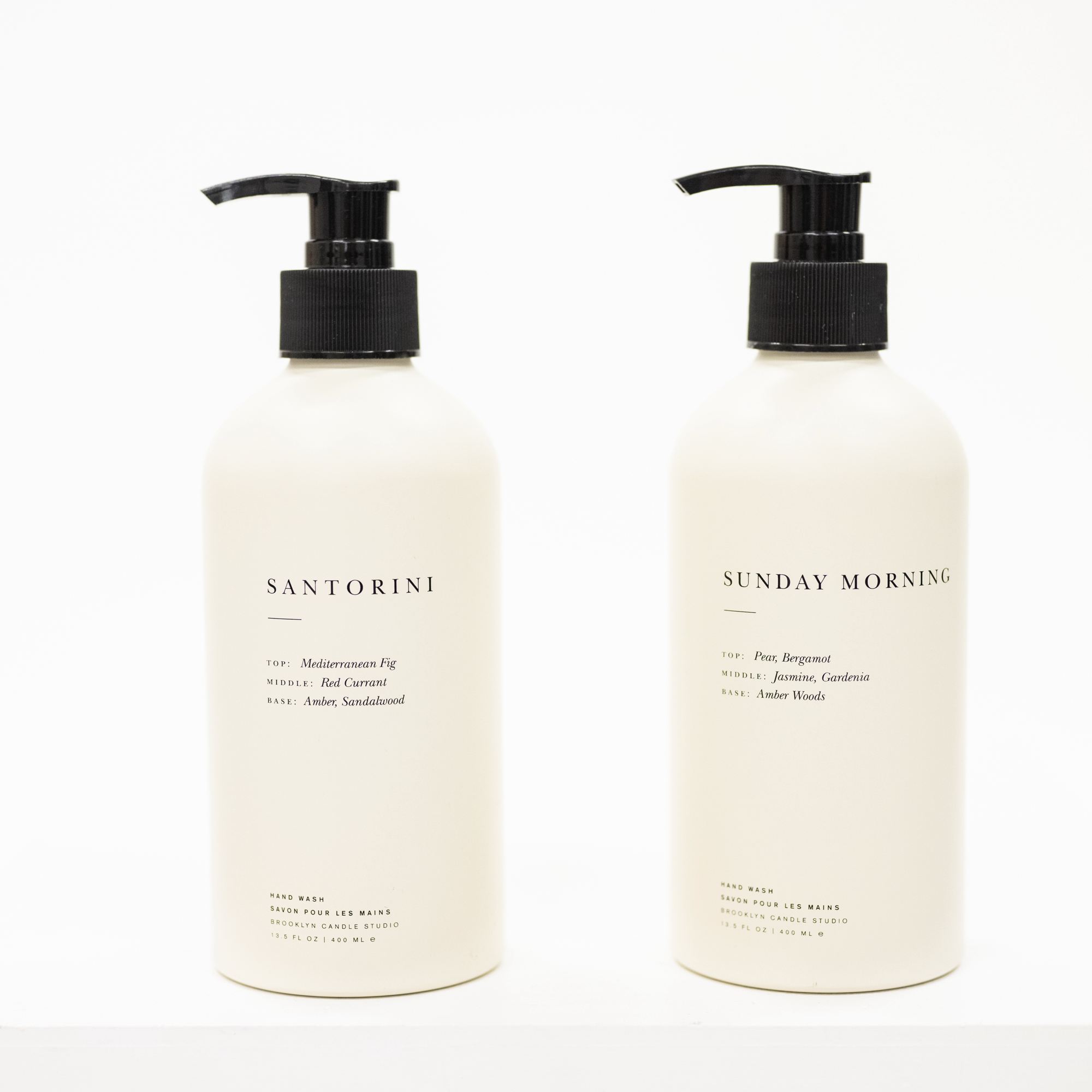 Two white bottles with black pump caps labeled 'Santorini' and 'Sunday Morning' on a white background.