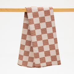 Checkered towel with brown and white pattern hanging on a wooden rod against a white background
