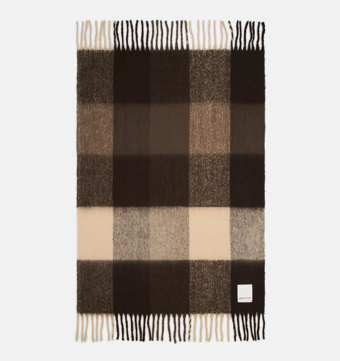A rectangular plaid scarf in shades of dark brown, medium brown, beige, and cream, featuring fringed ends and a small white brand label near the bottom right corner.