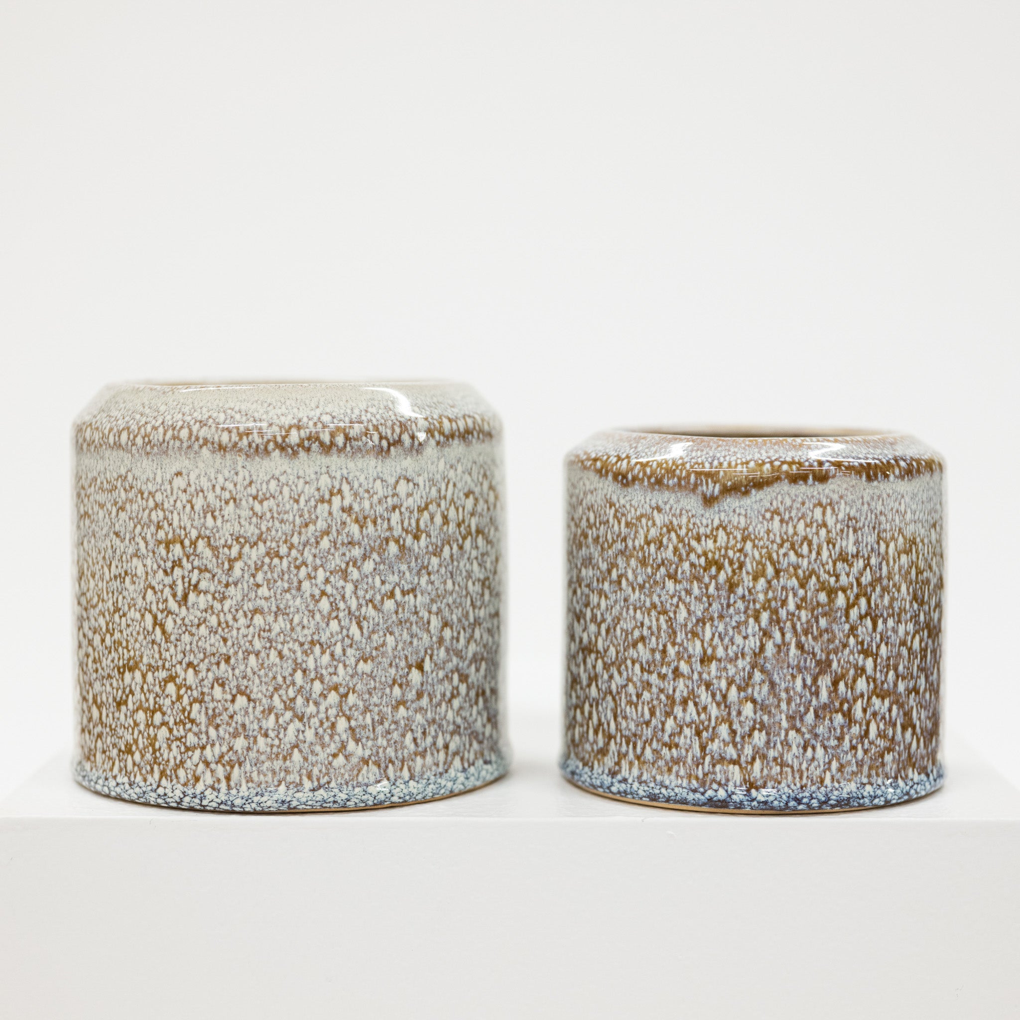 Two ceramic pots with brown and white 
textured surface on a white background