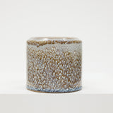 Cylindrical ceramic container with speckled glaze on a white background