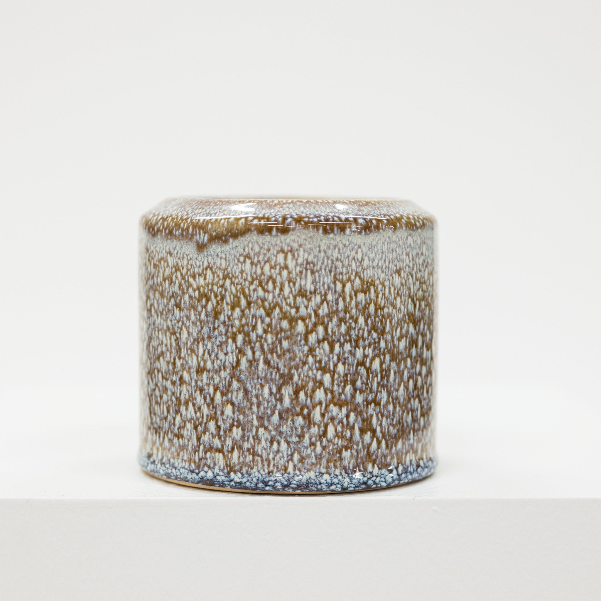 Cylindrical ceramic container with speckled glaze on a white background