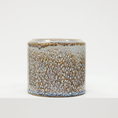 Cylindrical ceramic container with speckled glaze on a white background