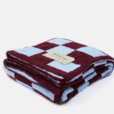 A folded plush fleece blanket with a checkered pattern in deep burgundy and light blue, featuring a beige brand label that reads 'ARCTIC FOX'.