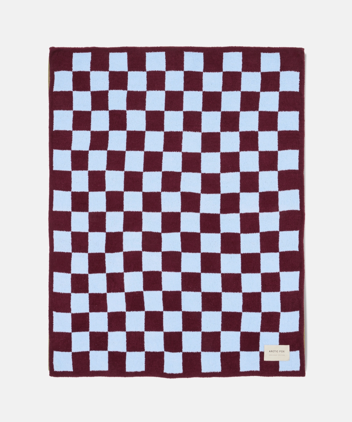 A rectangular plush blanket with a checkered pattern of deep burgundy and light blue squares, featuring a small beige brand tag in the bottom right corner.