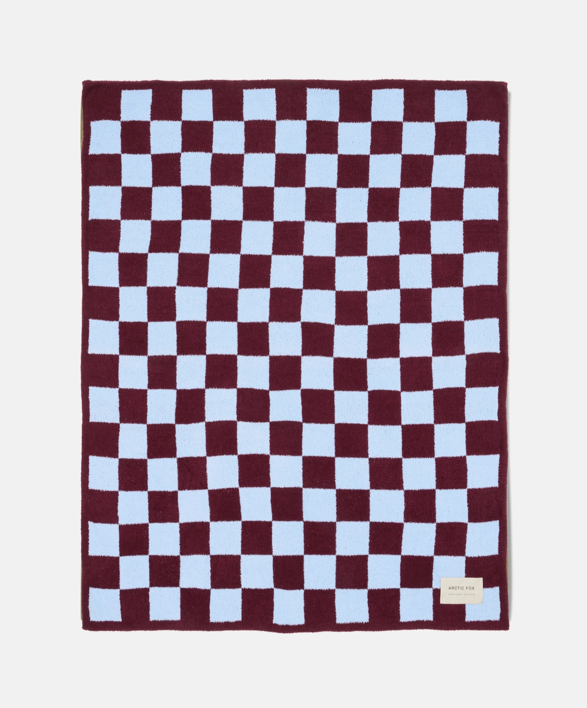 A rectangular plush blanket with a checkered pattern of deep burgundy and light blue squares, featuring a small beige brand tag in the bottom right corner.