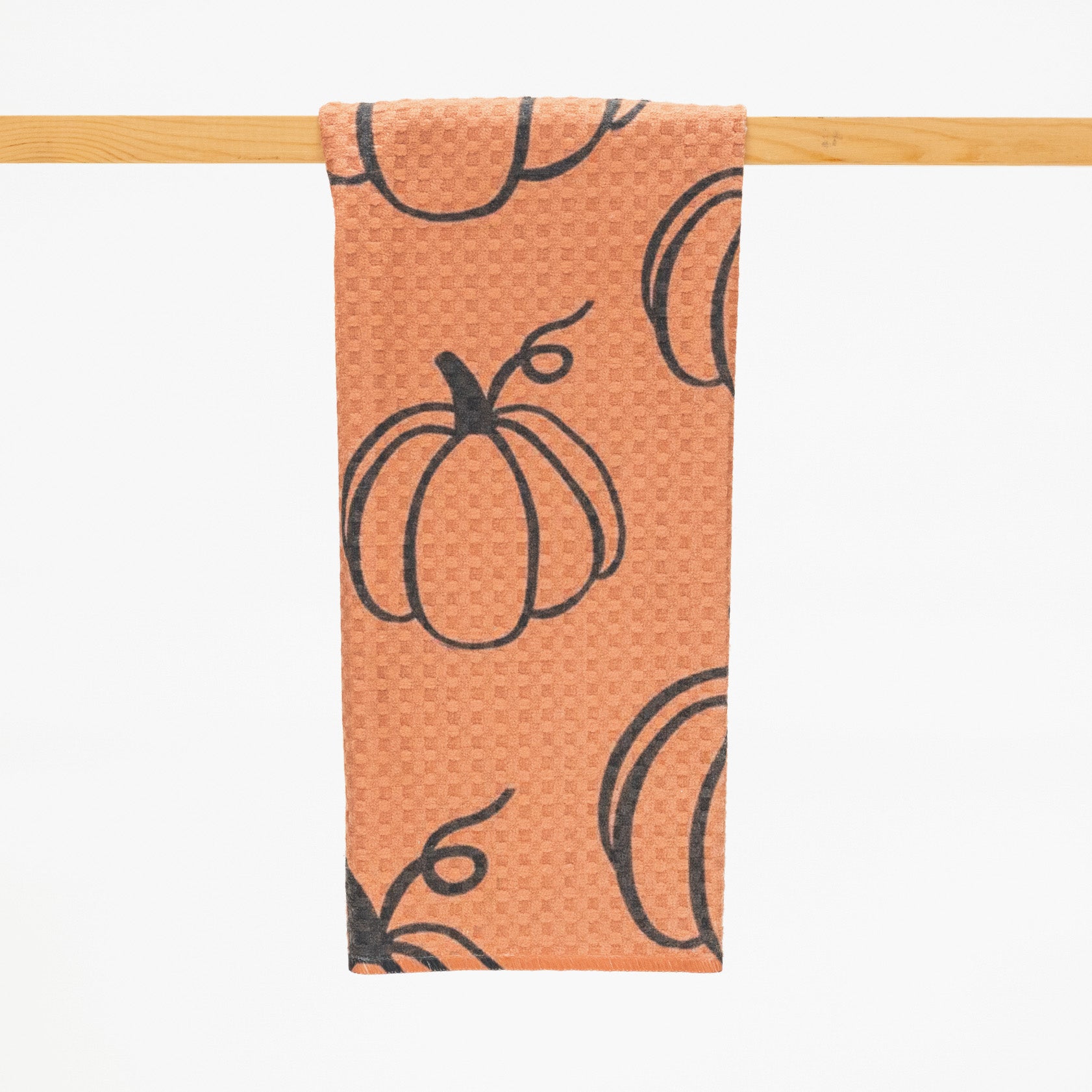 microfiber kitchen towel in burnt orange color with a pattern of repeated pumpkin outlines in black.