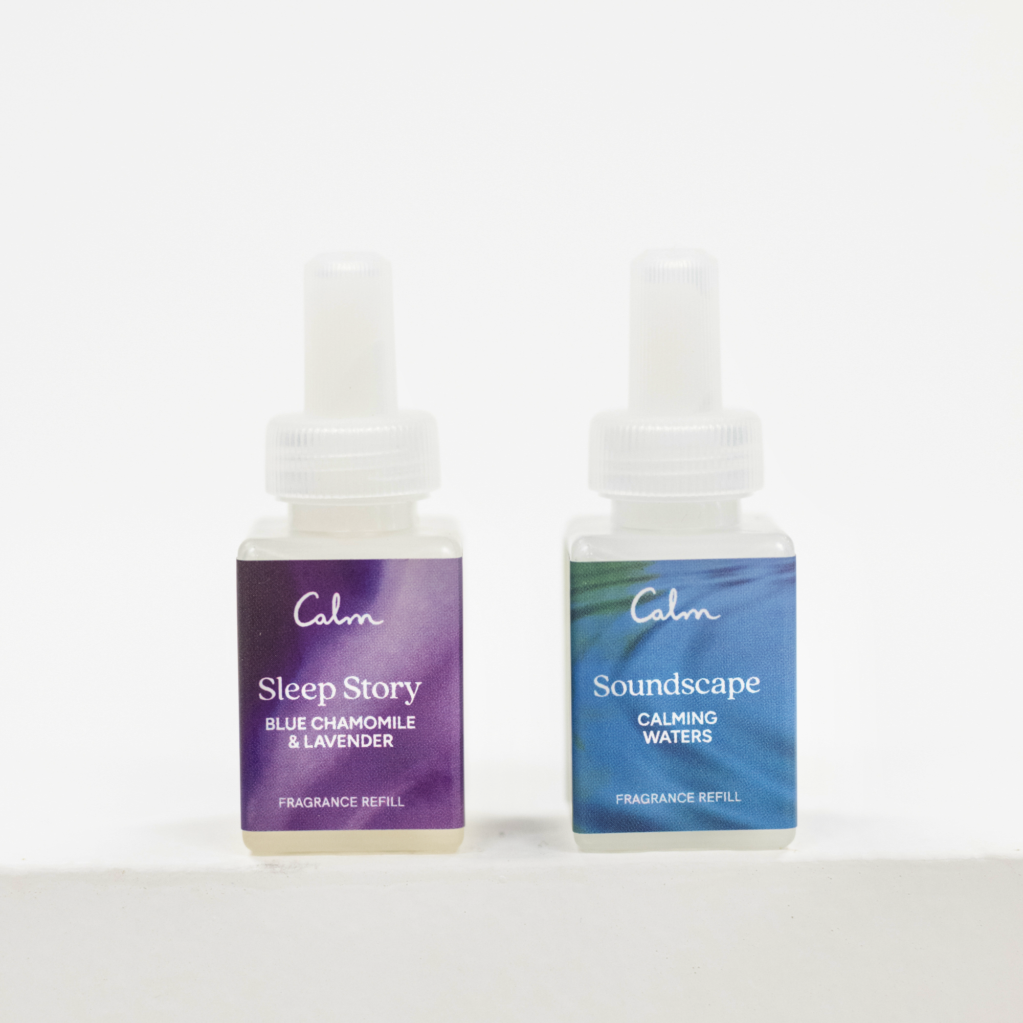 Two small fragrance refill bottles on a white surface against a white background. The left bottle has a purple label reading 'Calm Sleep Story Blue Chamomile & Lavender' and the right bottle has a blue-green label reading 'Calm Soundscape Calming Waters'.