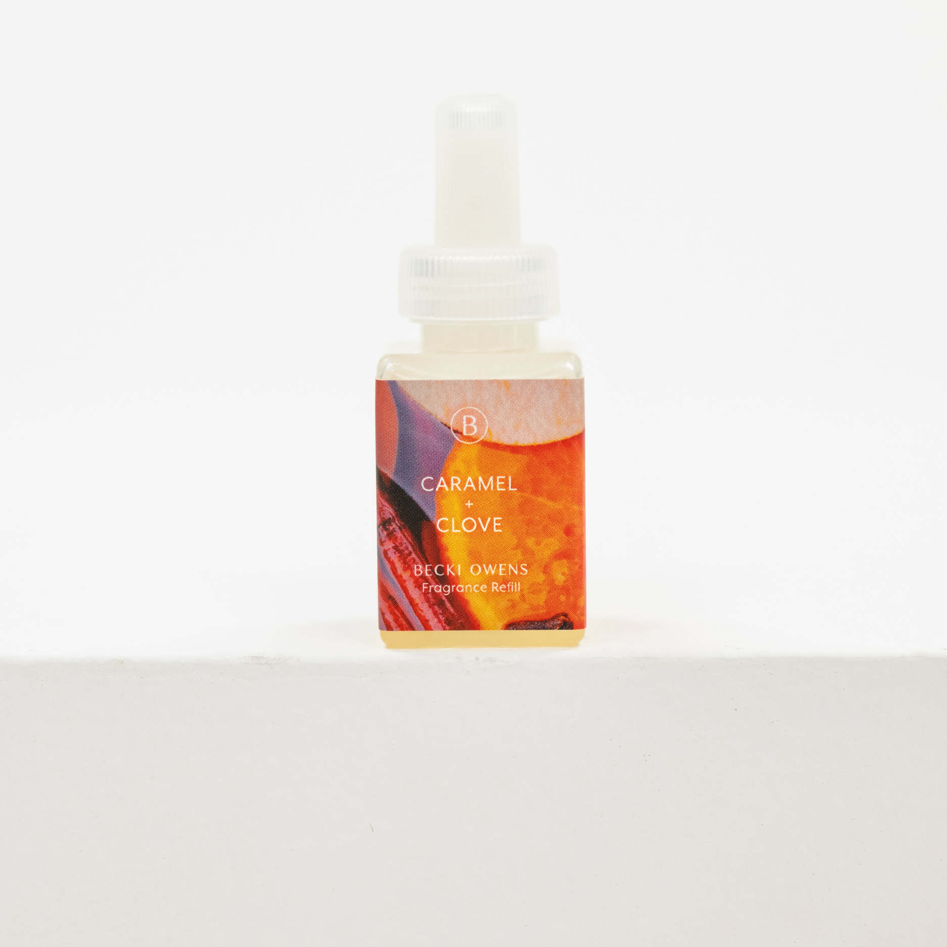 A small bottle of Becki Owens Caramel + Clove fragrance oil with a white dropper cap, set against a clean white background. Fall fragrance for Pura.
