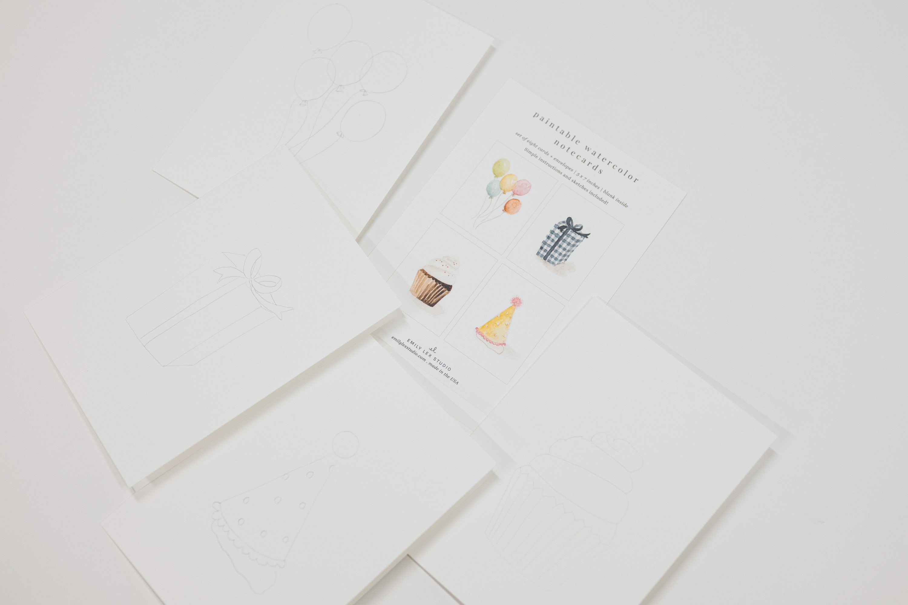 A set of white paper craft cards or envelopes arranged on a light gray background. One card shows faint line drawings, and another card displays small colorful illustrations including balloons, a cupcake, a hat, and a party hat with the text 'PARTY WIZARD'.