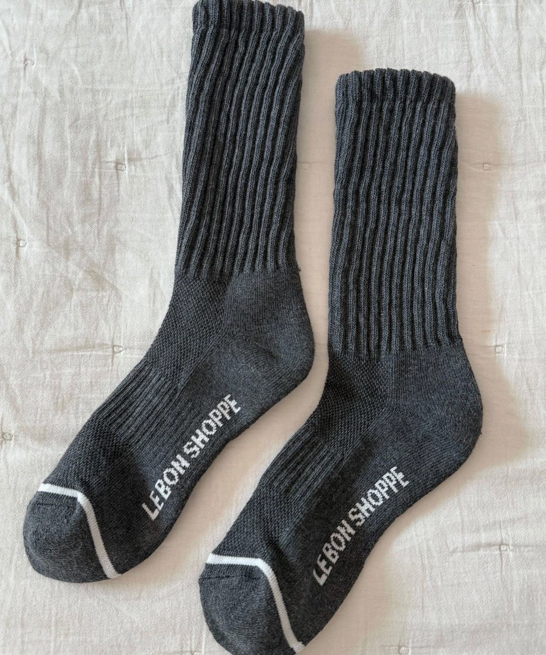 Pair of gray socks with 'Lebon Shoppe' branding on a textured beige surface