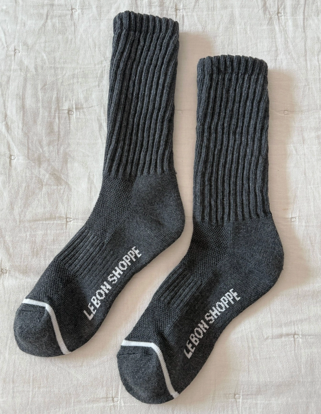 Pair of gray socks with 'Lebon Shoppe' branding on a textured beige surface