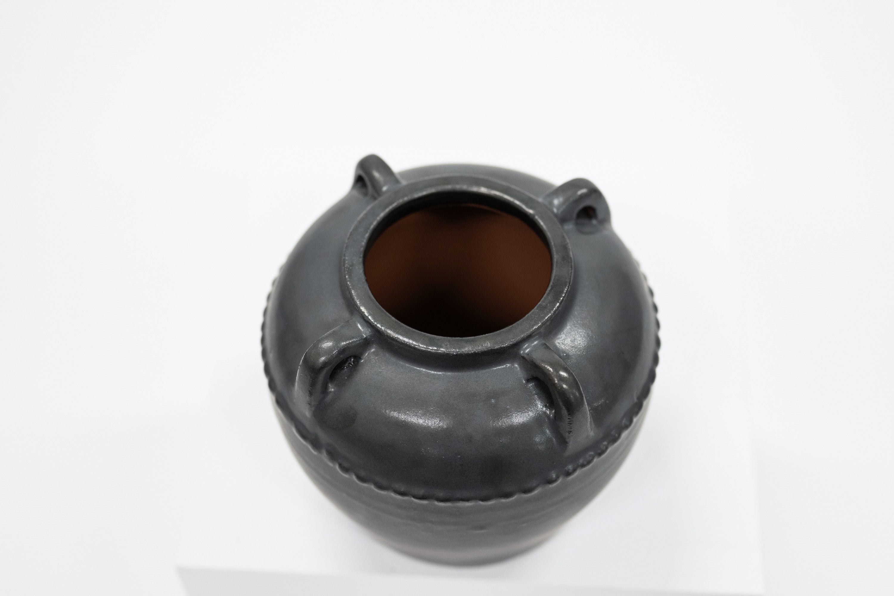 Black ceramic jar with three small handles on a white background