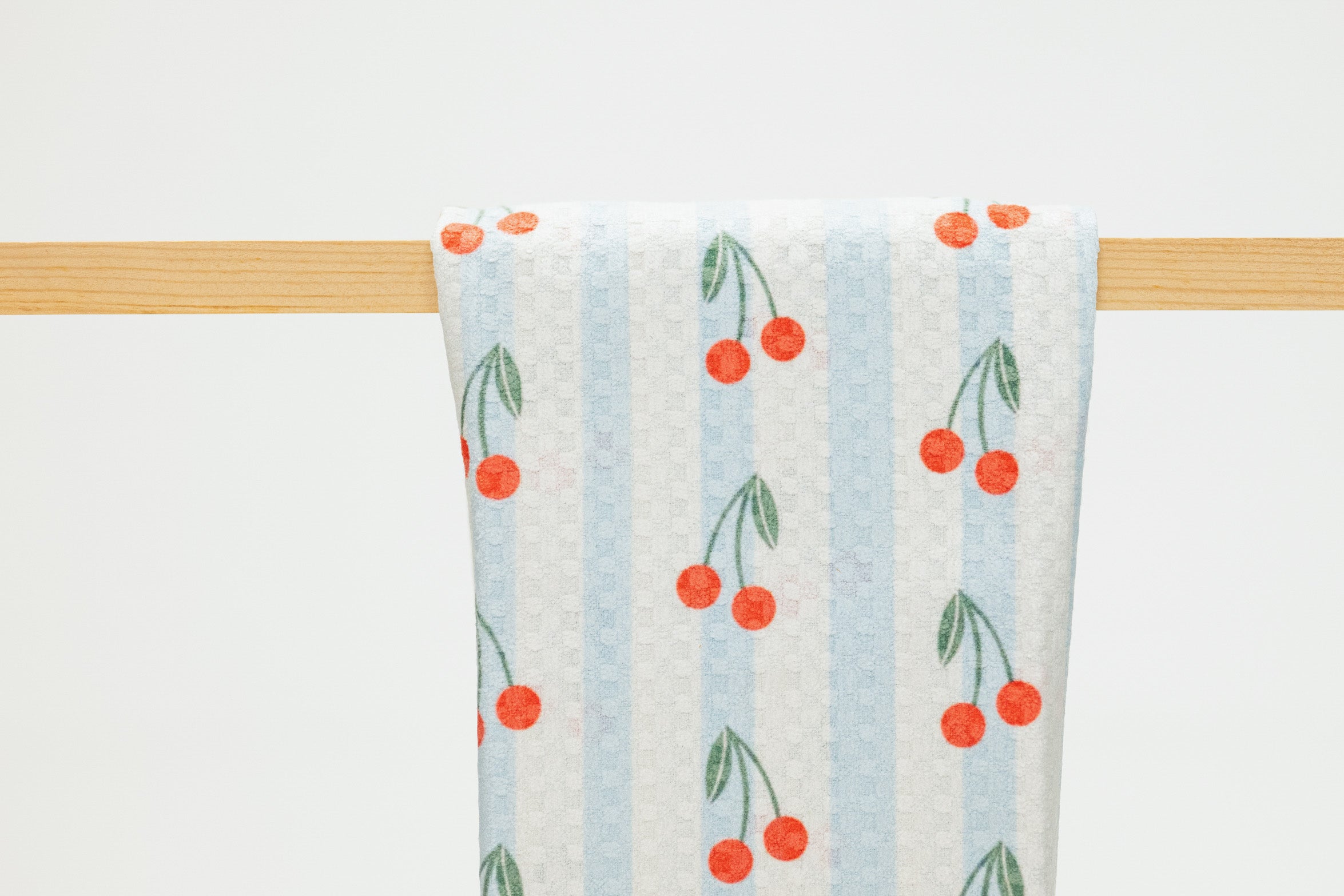 Towel with cherry pattern hanging on a wooden rack against a white background