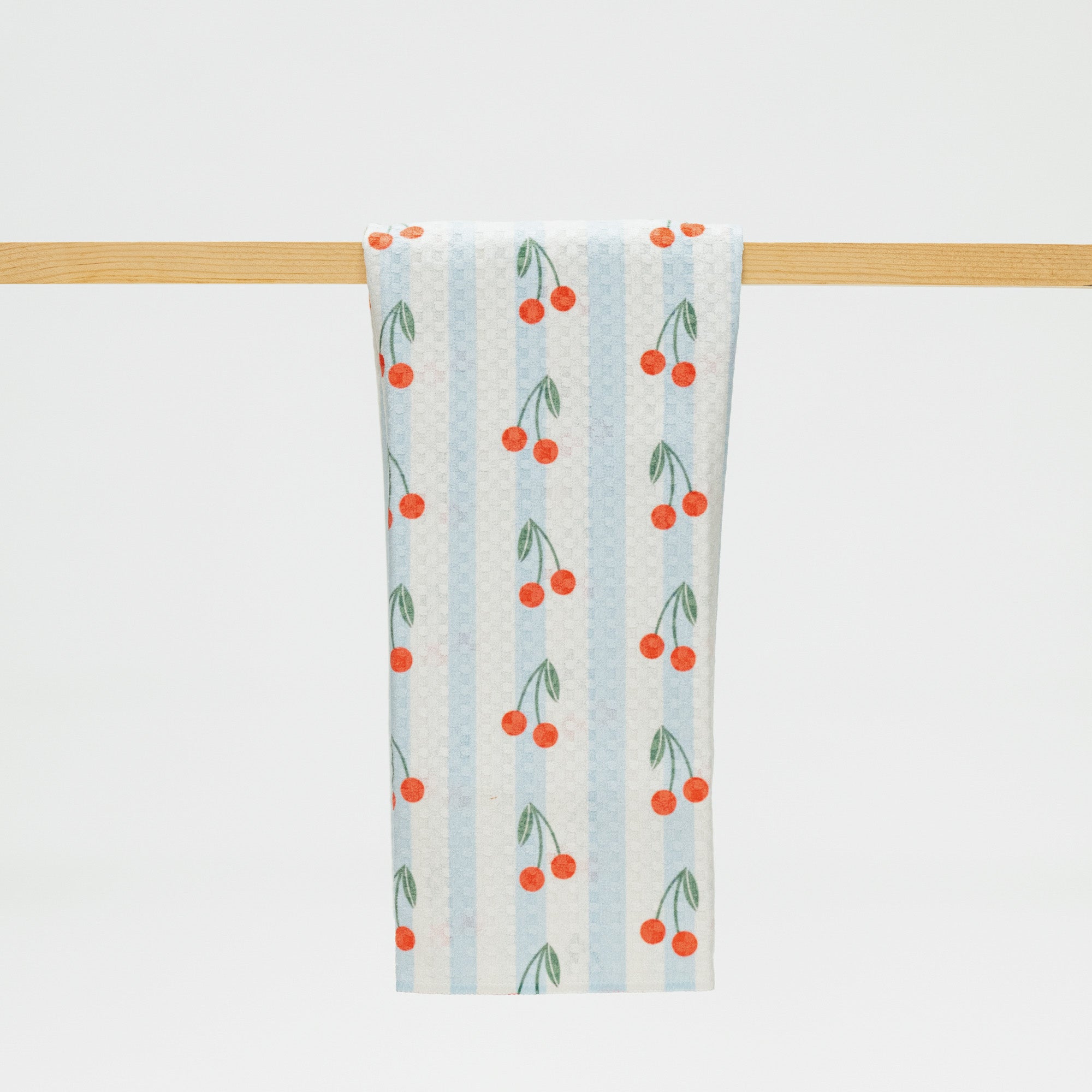 Towel with cherry pattern hanging on a wooden rack against a white background