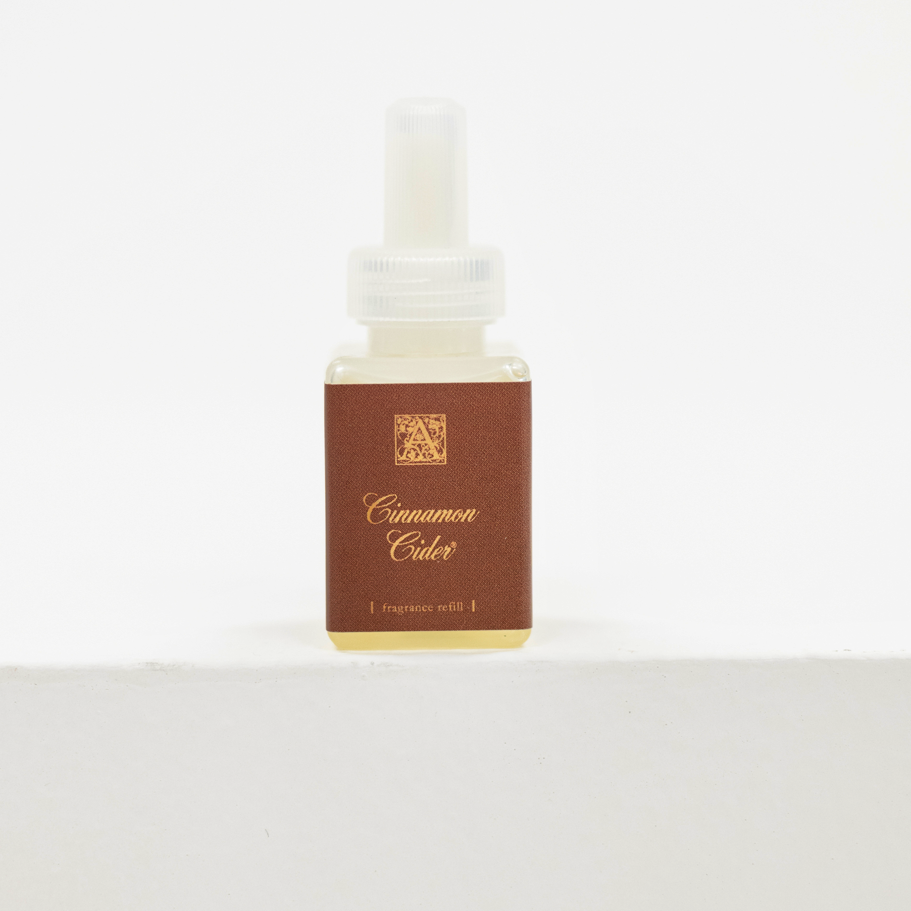 A small square bottle of Cinnamon Cider fragrance oil with a white dropper cap and a brown label, set against a plain white background. Fall scent for Pura.
