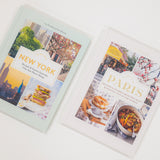 Two travel guidebooks on New York and Paris with images of cityscapes and food.