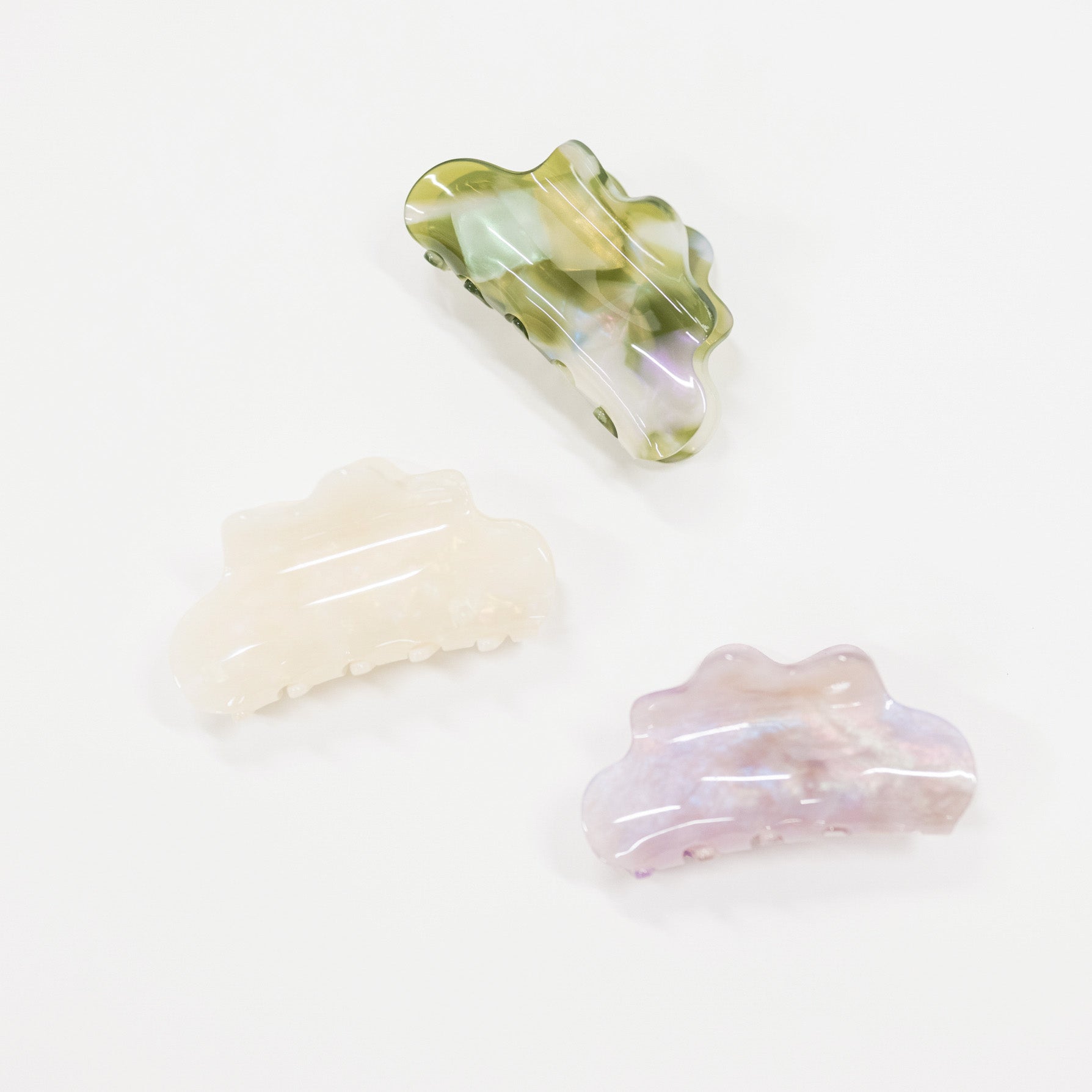 Three iridescent hair claw clips in different colors (green, cream, and lavender) arranged on a plain white background.