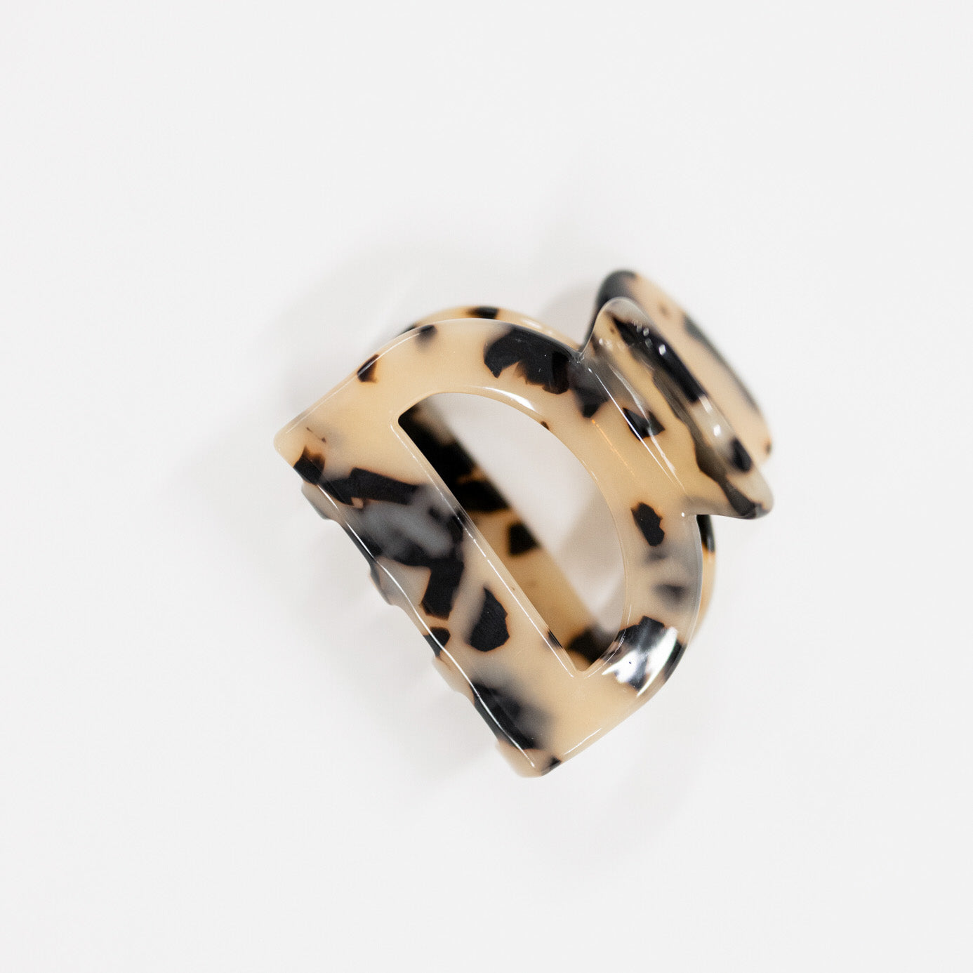 A large claw hair clip in a glossy tortoiseshell pattern, featuring a beige base with black and brown spots, photographed on a clean white background.
