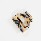 A large claw hair clip in a glossy tortoiseshell pattern, featuring a beige base with black and brown spots, photographed on a clean white background.