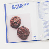 Open cookbook showing a recipe for Black Forest Cookies with two cookies displayed.