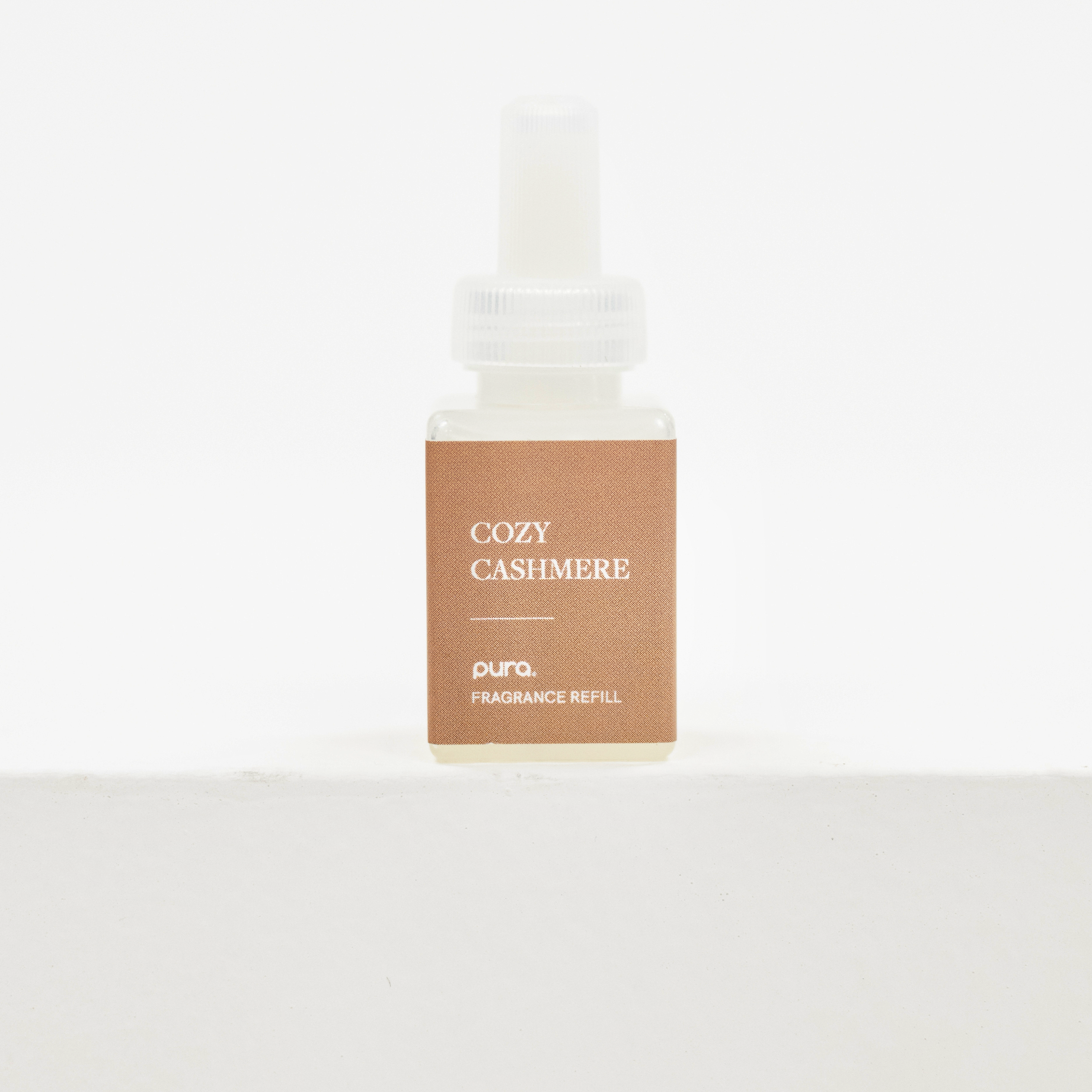A small rectangular fragrance refill bottle with a white dropper cap and a tan label reading 'COZY CASHMERE' and 'pura. FRAGRANCE REFILL', centered on a clean white background. Fall scent for Pura.
