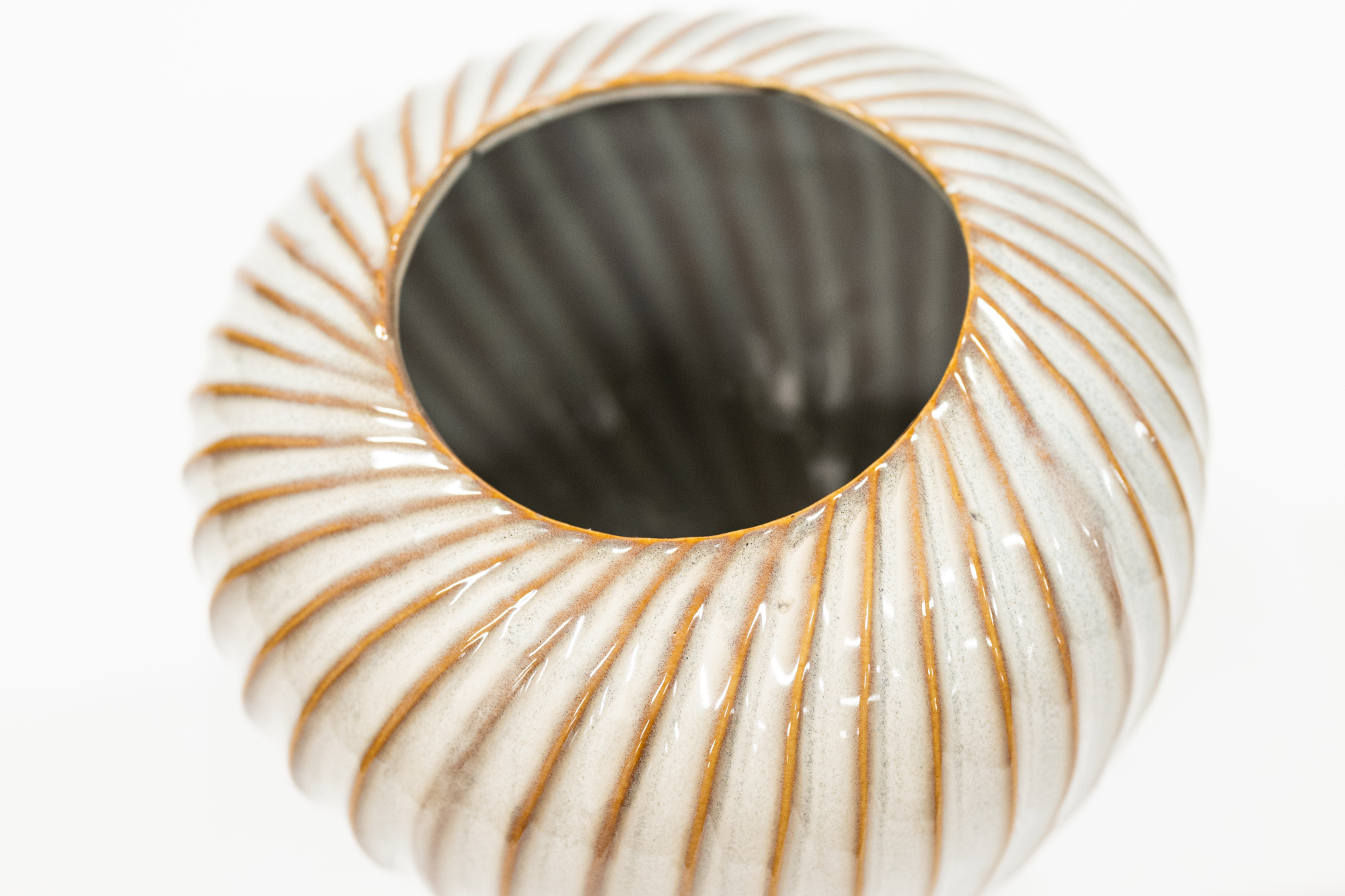 A close-up of a ribbed ceramic planter or vase with a glossy off-white glaze and warm brown edging, shown against a plain white background.