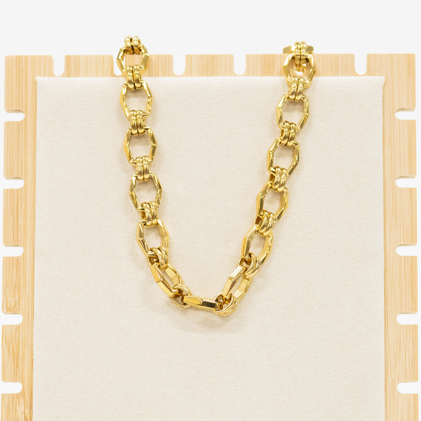 Gold chain necklace on a wooden stand with a white background