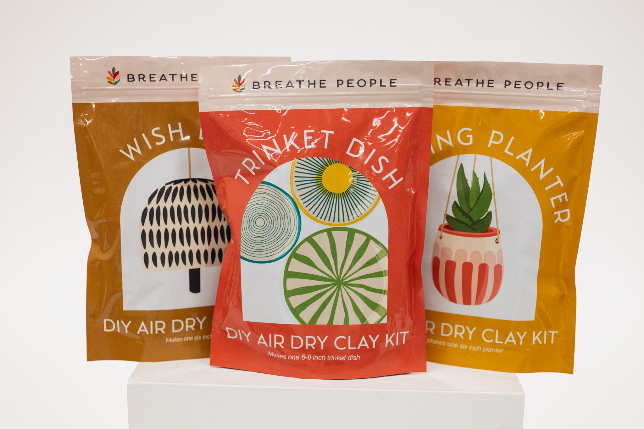 Three air dry clay kit packages with illustrations and text on a white background