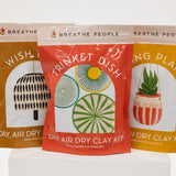 Three air dry clay kit packages with illustrations and text on a white background