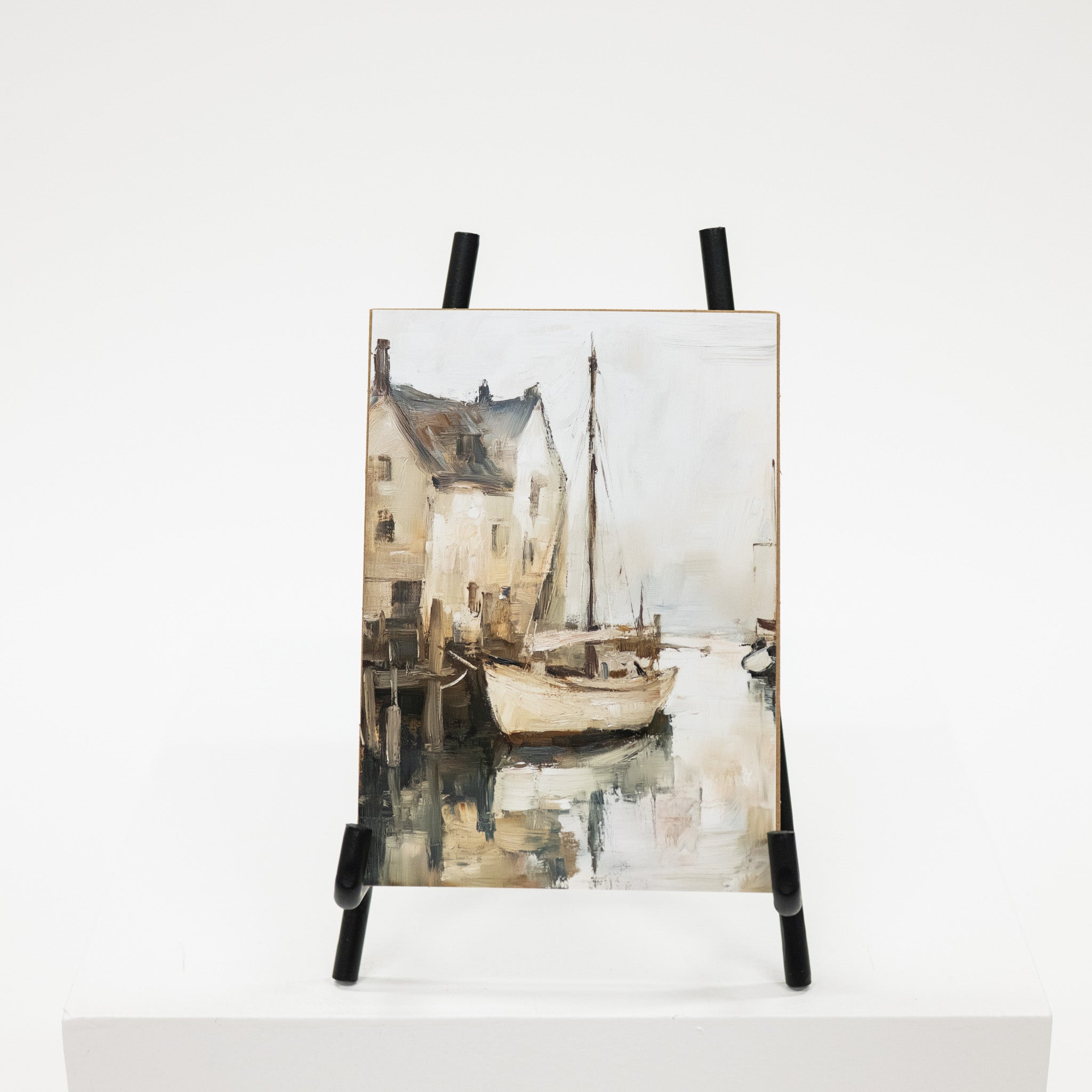 Art print of a coastal scene with a sailboat on an easel against a white background