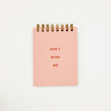 A pink spiral-bound notepad with the words 'DON'T RUSH ME' printed in red on the front, photographed against a plain white background.