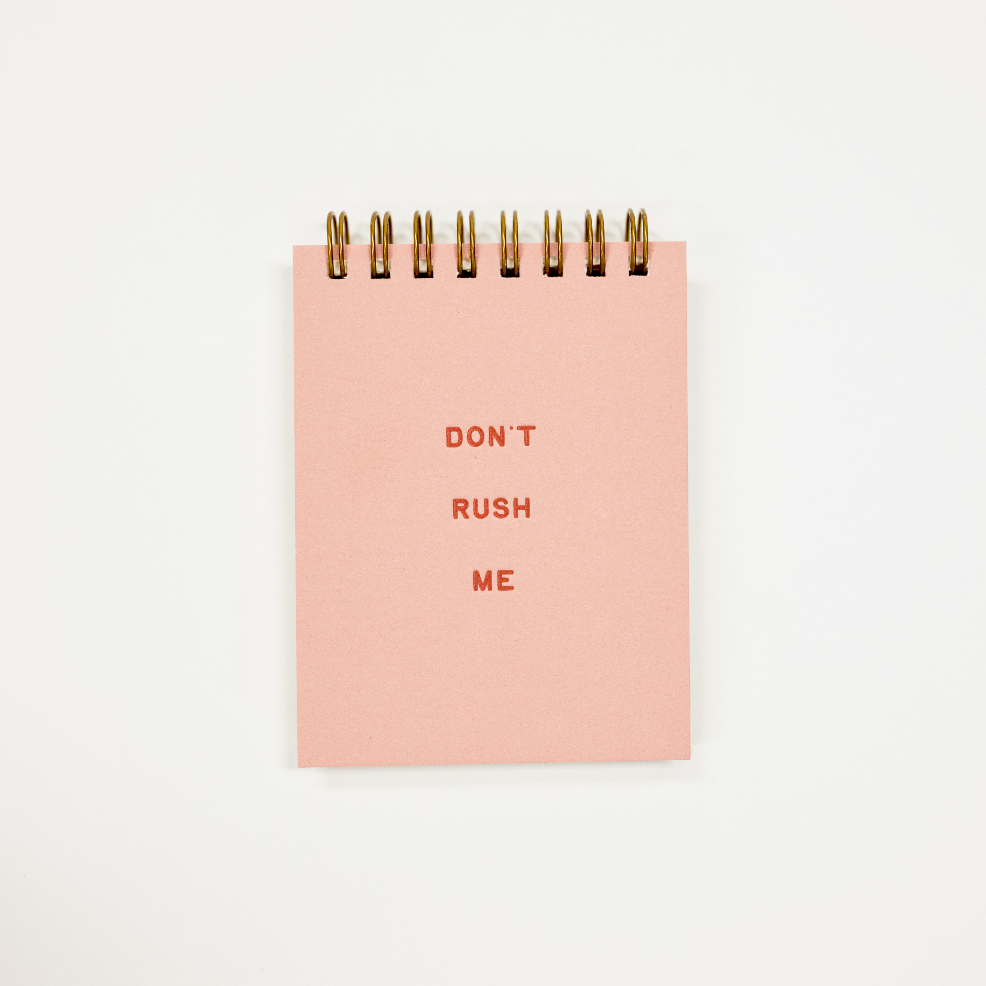 A pink spiral-bound notepad with the words 'DON'T RUSH ME' printed in red on the front, photographed against a plain white background.