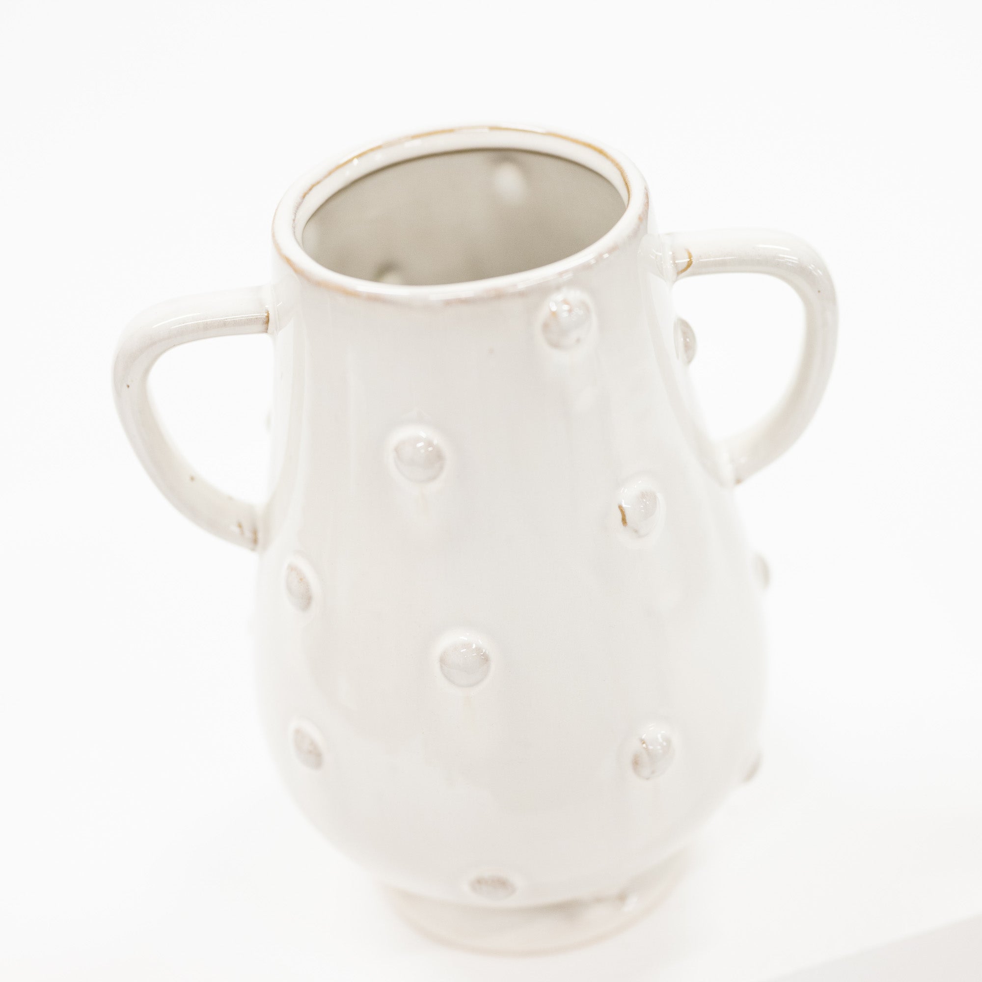 A white ceramic pitcher with two side handles and a textured, dimpled surface, photographed against a seamless white background.