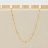 Gold chain necklace on a beige cushion with a wooden base