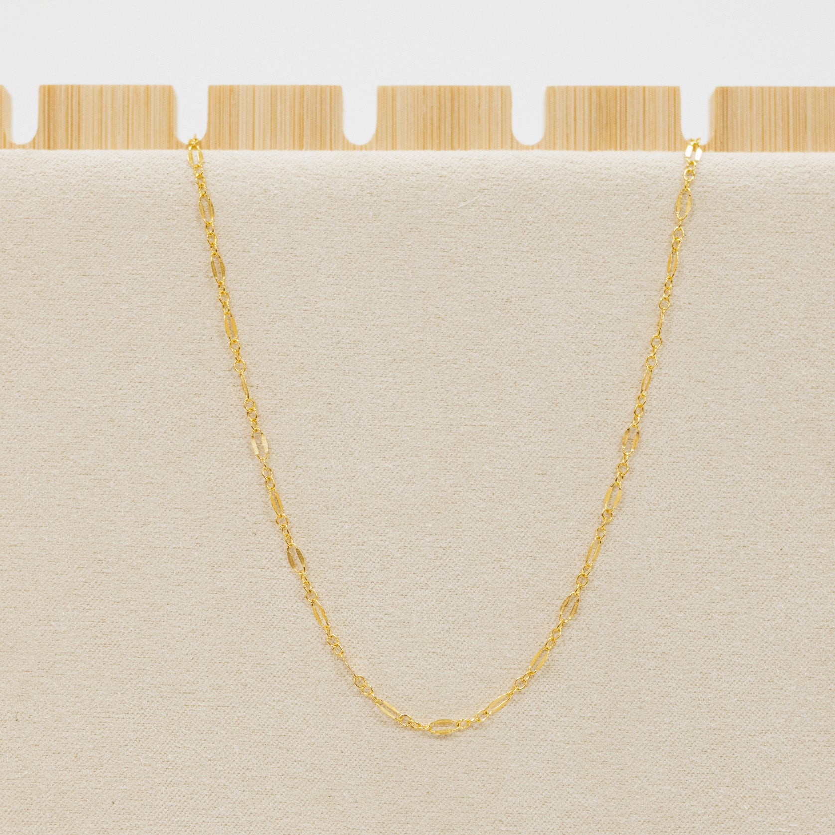 Gold chain necklace on a beige cushion with a wooden base