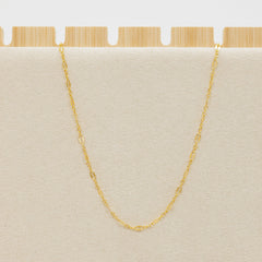 Gold chain necklace on a beige cushion with a wooden base