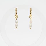 A pair of gold huggie hoop earrings with dangling baroque pearls, displayed on a clean white circular background.