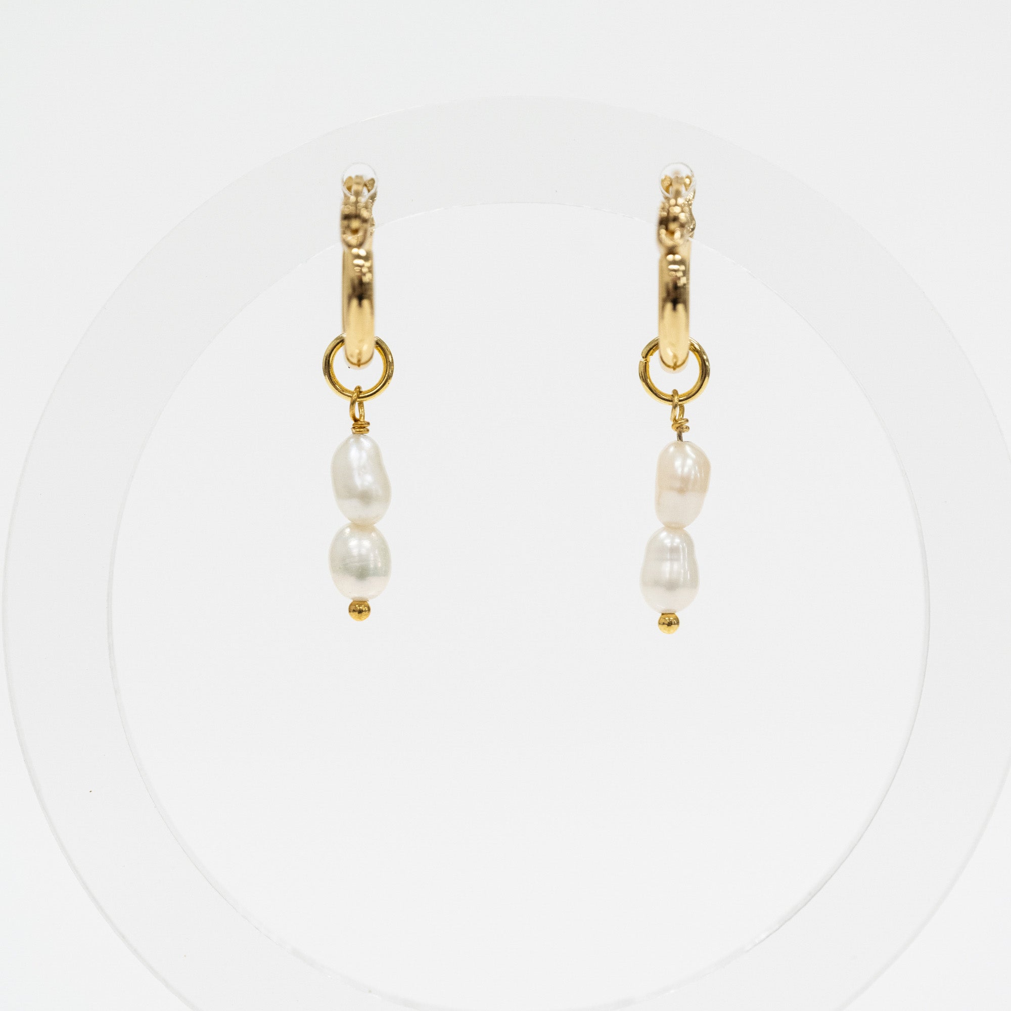 A pair of gold huggie hoop earrings with dangling baroque pearls, displayed on a clean white circular background.