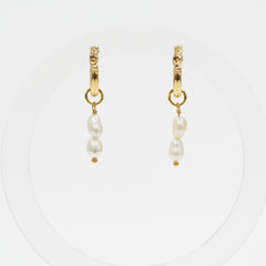 A pair of gold huggie hoop earrings with dangling baroque pearls, displayed on a clean white circular background.