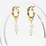 Gold hoop earrings with dangling white pearl beads, displayed on a clear acrylic stand against a white background.