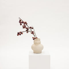 White vase with dried branches on a white pedestal against a white background
