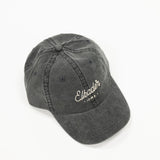 charcoal black colored dad style baseball hat. includes white colored script lettering to spell "elkader" 