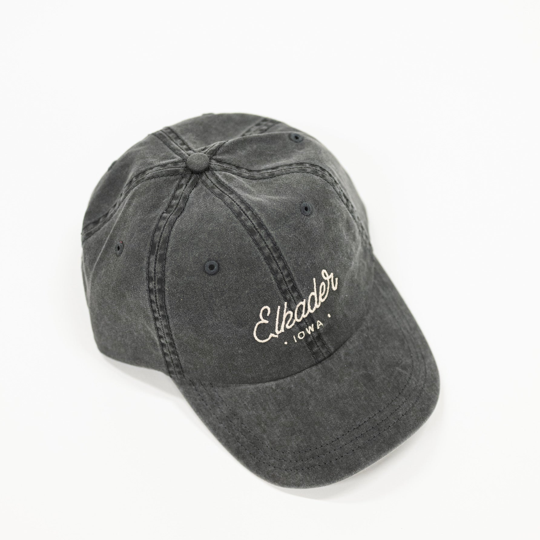 charcoal black colored dad style baseball hat. includes white colored script lettering to spell "elkader" 