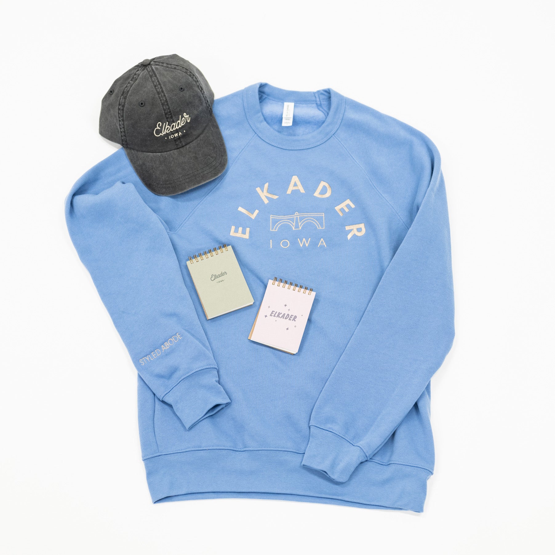 Elkader custom products including sweatshirt, dad hat and small notepad.