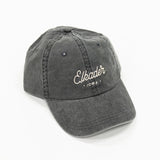 charcoal black colored dad style baseball hat. includes white colored script lettering to spell "elkader" 