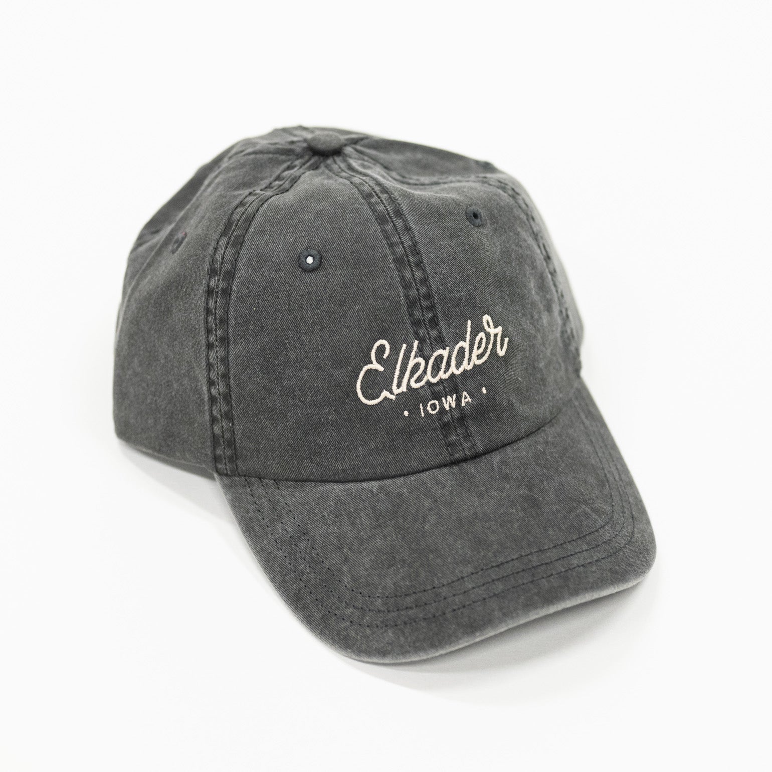 charcoal black colored dad style baseball hat. includes white colored script lettering to spell "elkader" 