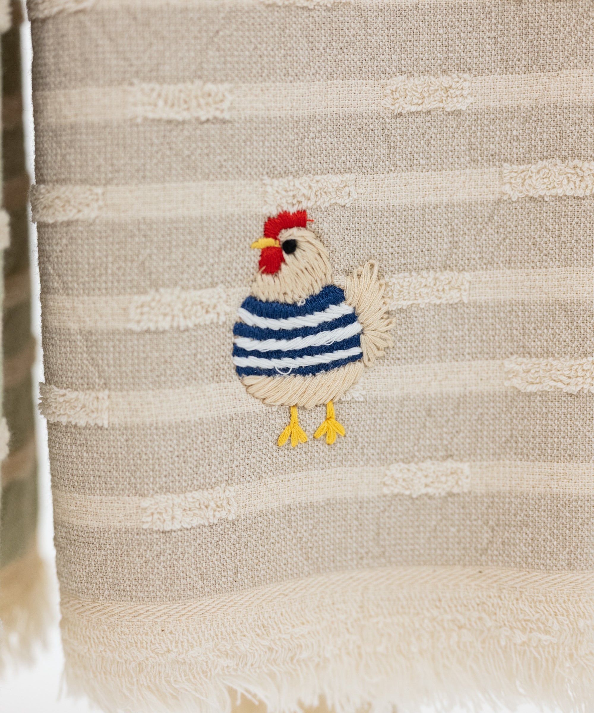 taupe and cream striped turkish cotton towel with fringe and embroidered chicken wearing a blue sweater.