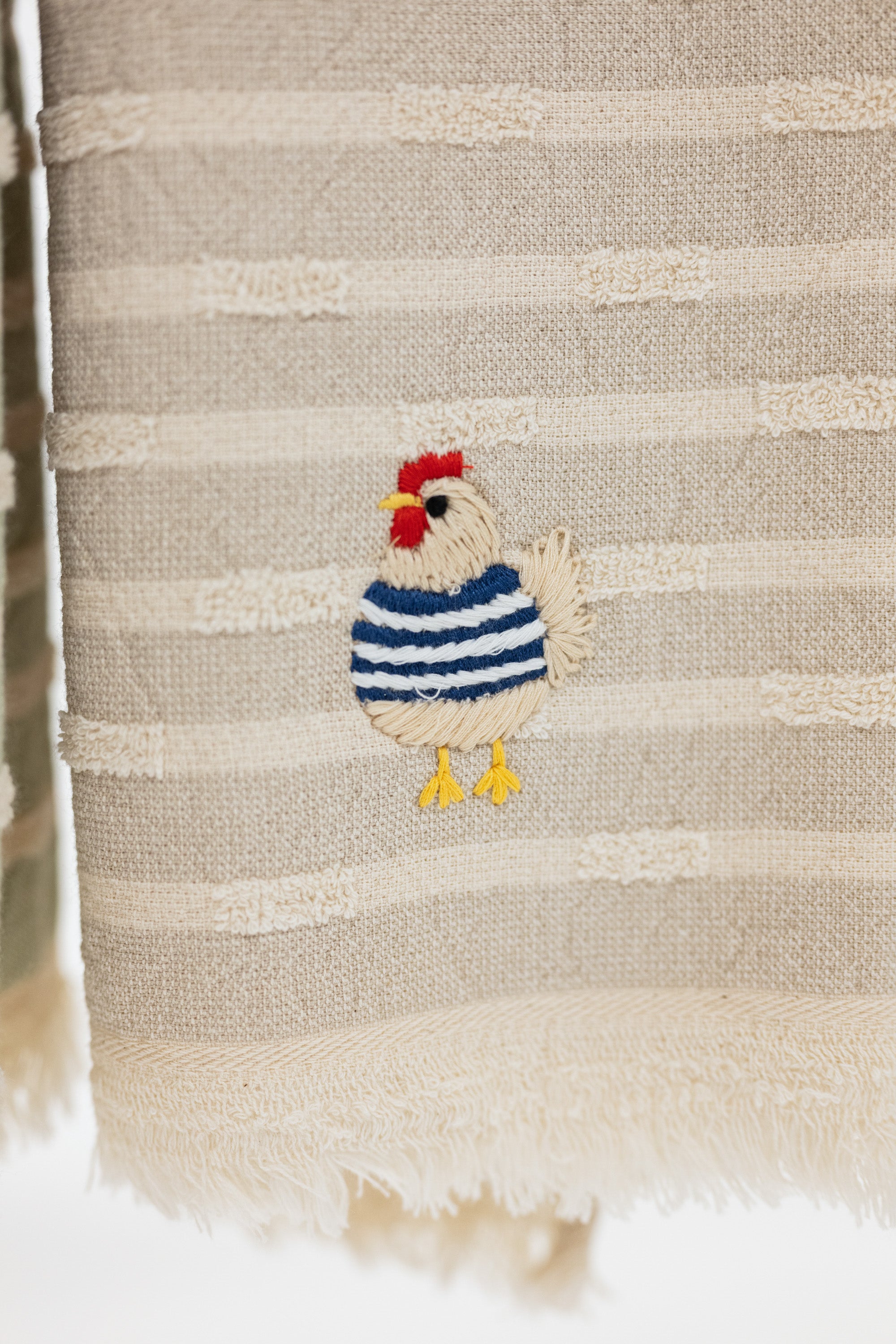 taupe and cream striped turkish cotton towel with fringe and embroidered chicken wearing a blue sweater.